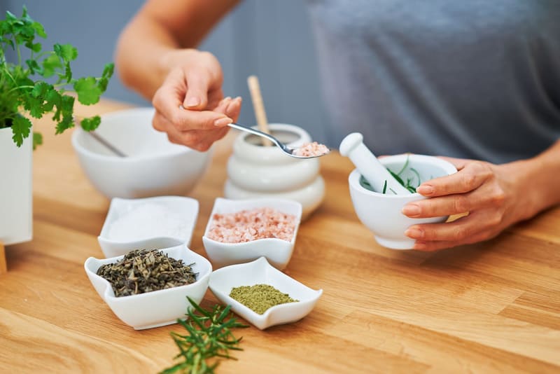 Manos preparando cosmética casera con hierbas secas, sal y mortero
