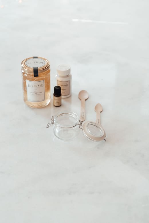 Ingredientes y utensilios para hacer cosmética casera: tarro de cristal, frasquito y cucharas de madera sobre mármol