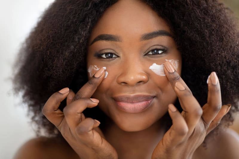 Mujer sonriente aplicándose crema natural en las mejillas